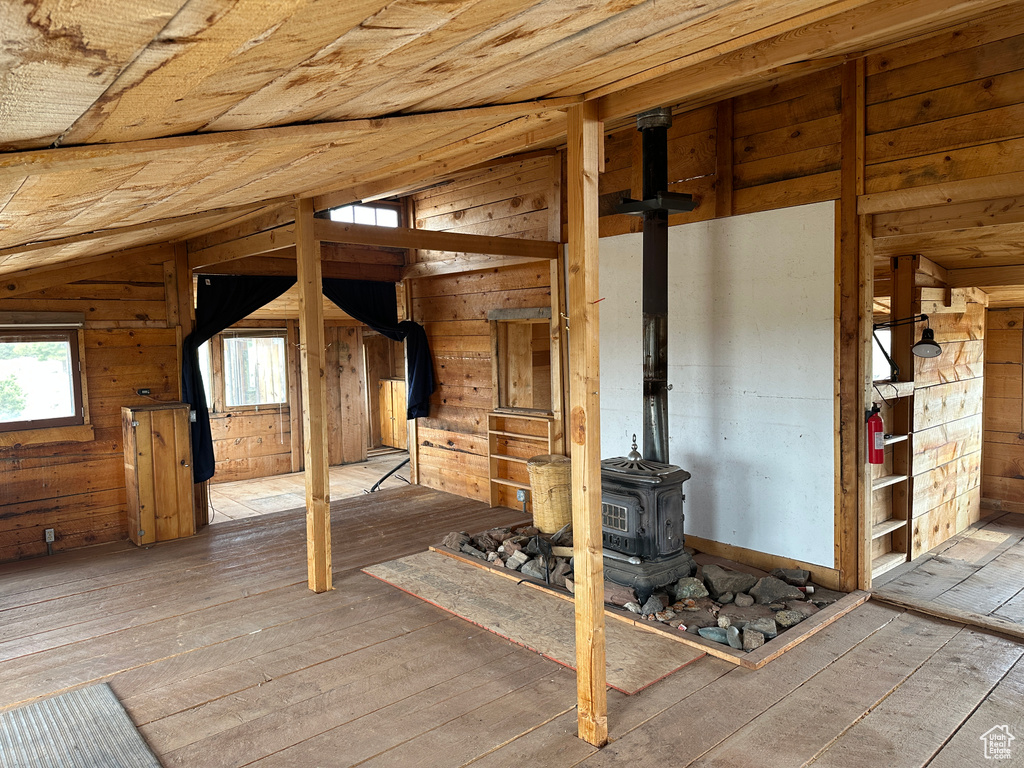 Empty room featuring a wood stove, lofted ceiling, hardwood / wood-style flooring, and wood walls