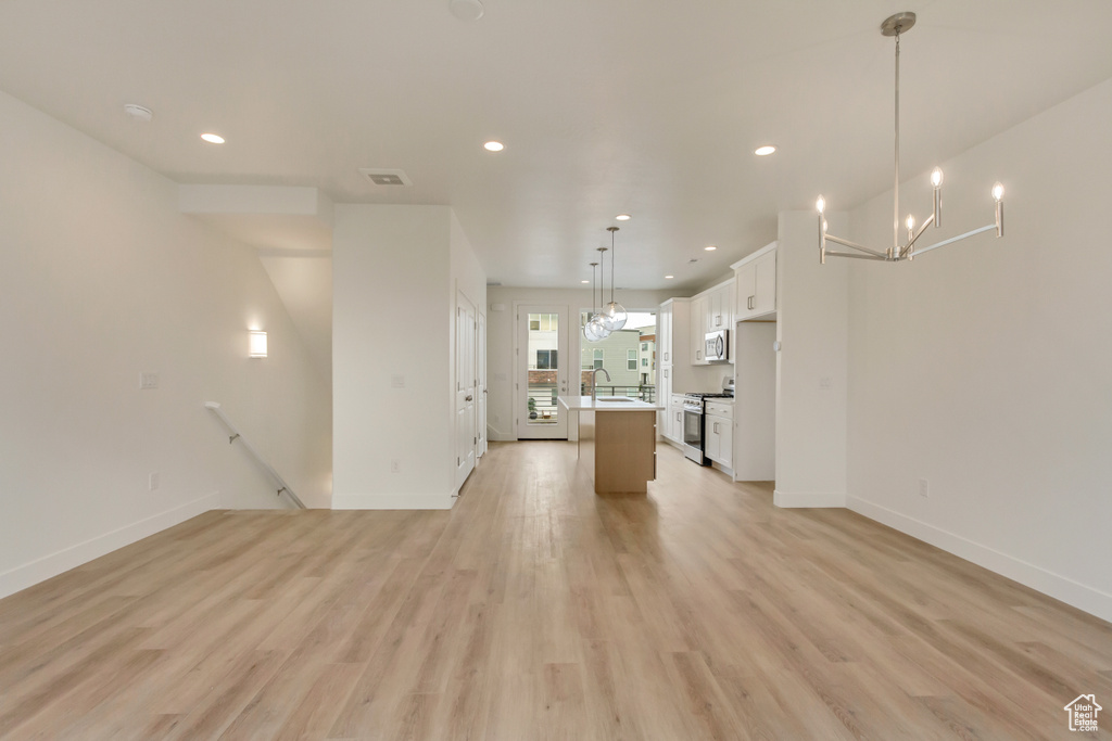 Unfurnished living room with recessed lighting, light wood finished floors, a chandelier, a sink, and baseboards