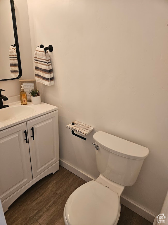 Half bathroom featuring wood finished floors, toilet, vanity, and baseboards