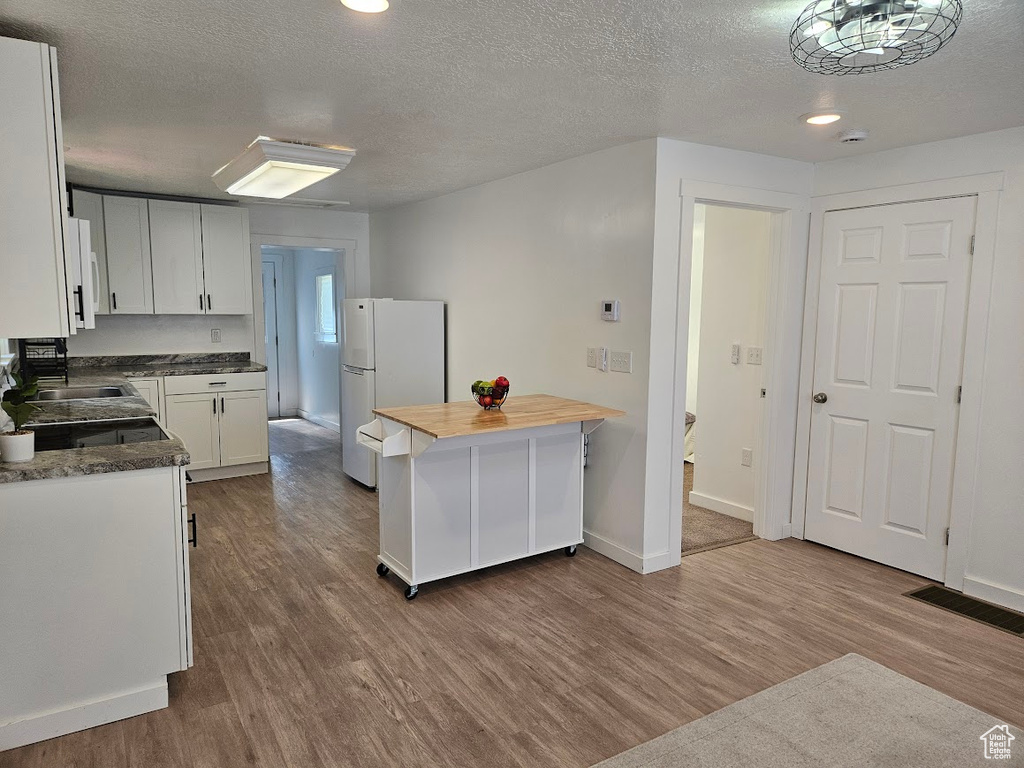 Kitchen featuring freestanding refrigerator, wood counters, dark wood-style floors, a textured ceiling, and white cabinetry