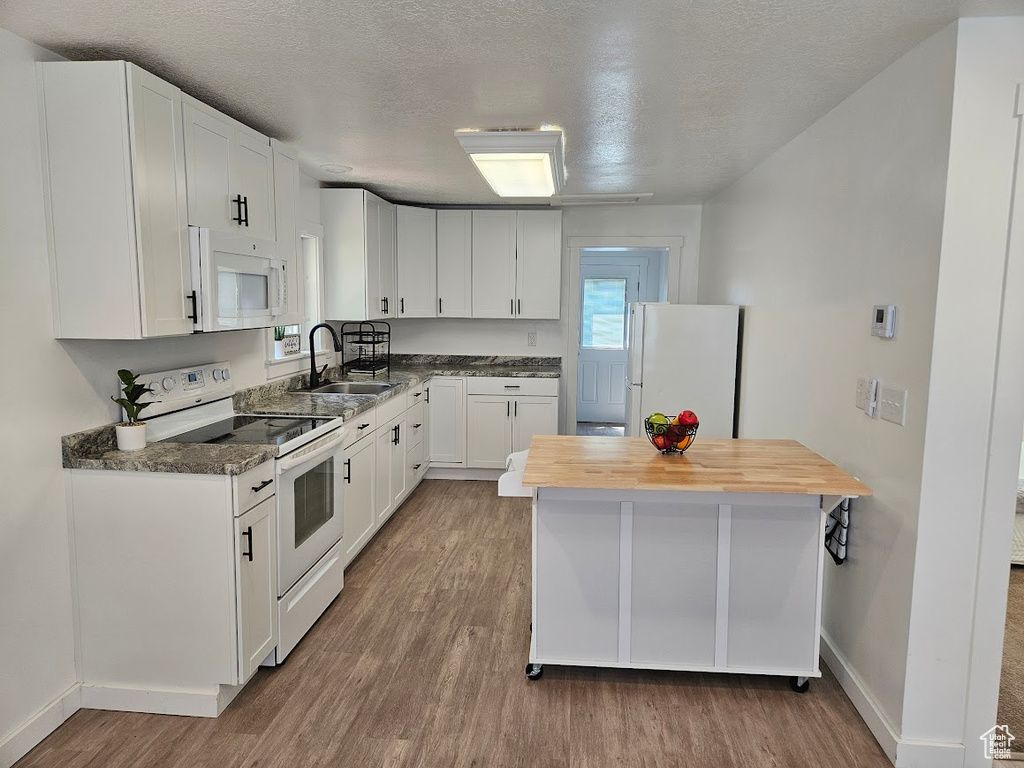 Kitchen featuring white appliances, a sink, wood finished floors, wooden counters, and white cabinets