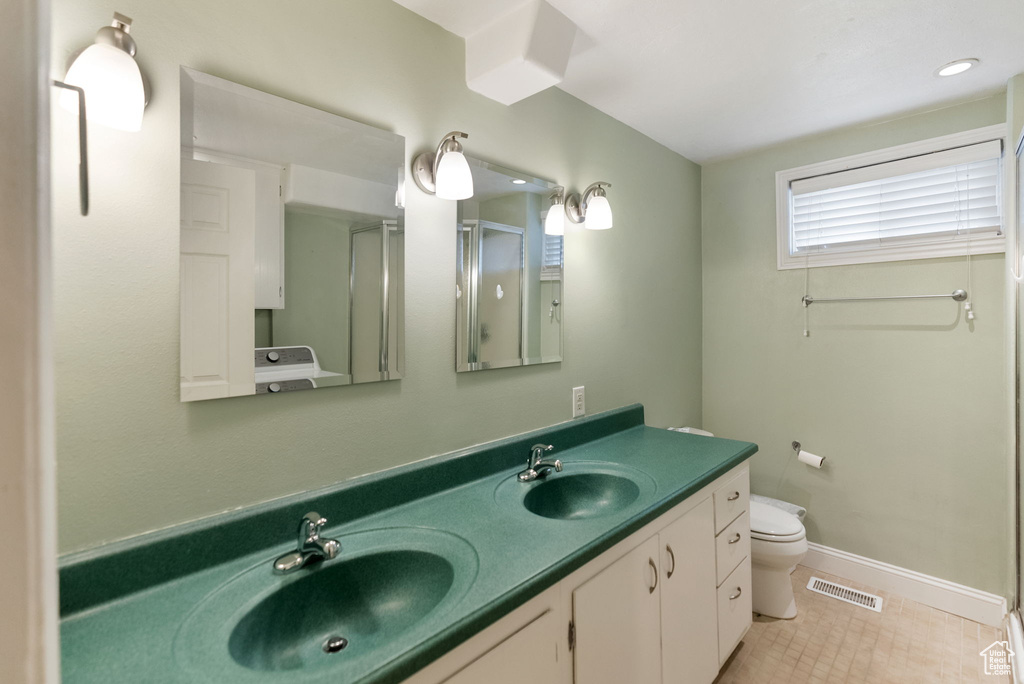 Bathroom featuring toilet, double vanity, a stall shower, baseboards, and tile patterned flooring