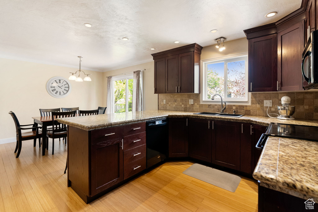 Kitchen with black appliances, a sink, a peninsula, light wood-type flooring, and backsplash