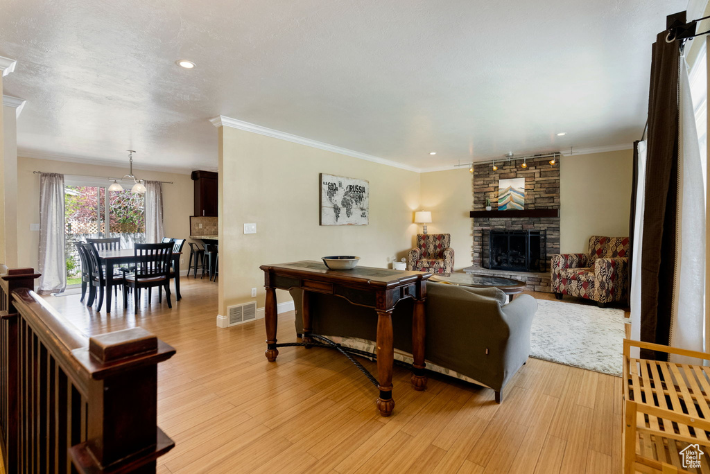 Living room with a fireplace, light wood-type flooring, crown molding, baseboards, and recessed lighting