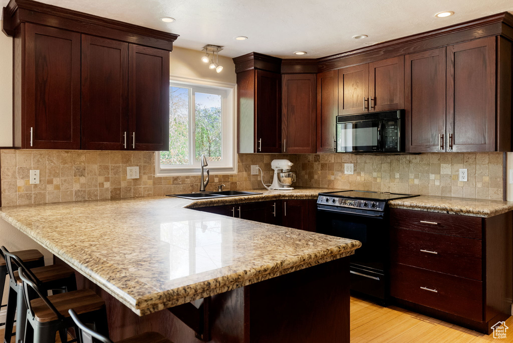 Kitchen with black appliances, a sink, a peninsula, a breakfast bar area, and decorative backsplash
