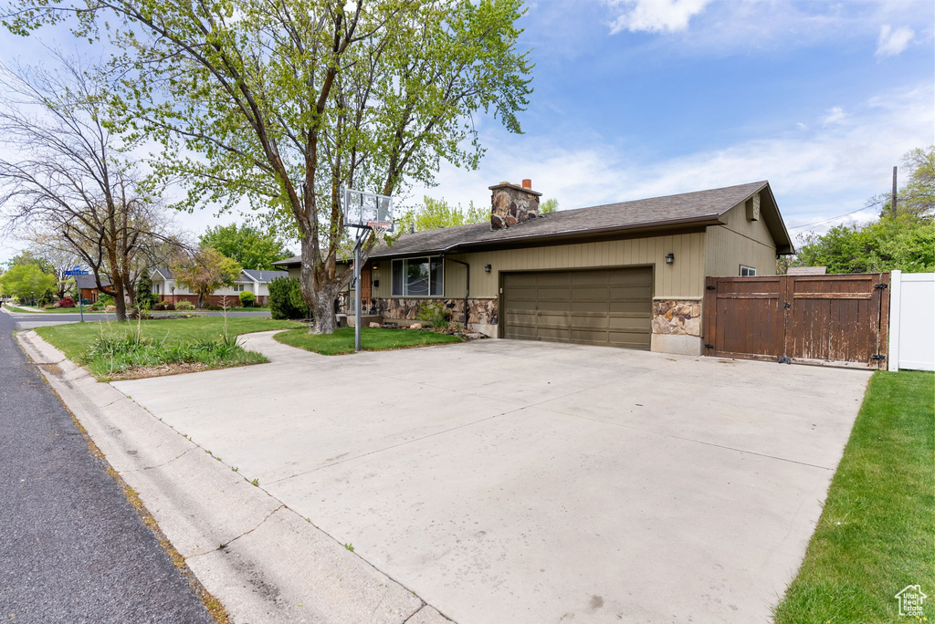 View of front of house featuring stone siding, a gate, a garage, concrete driveway, and a chimney