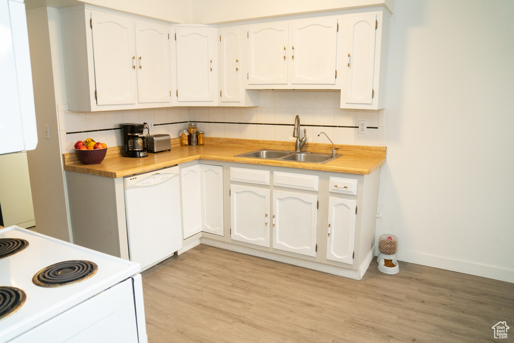 Kitchen with a sink, white appliances, decorative backsplash, white cabinets, and light wood finished floors