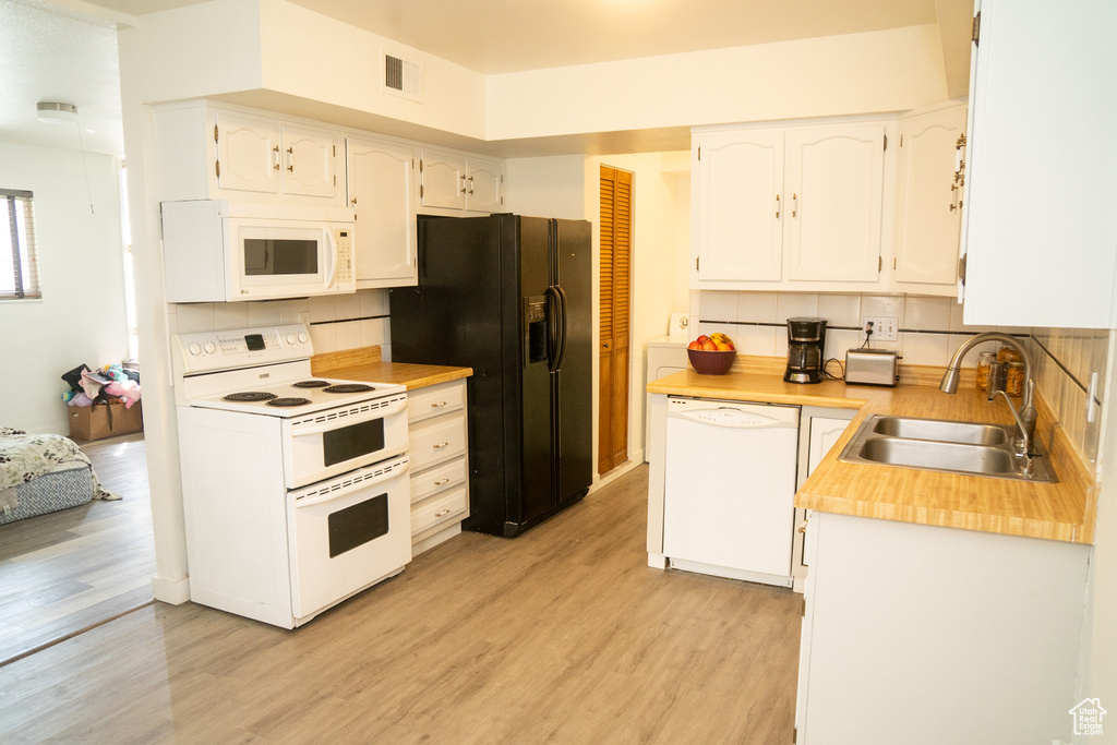 Kitchen with white appliances, a sink, light wood-style floors, white cabinets, and backsplash