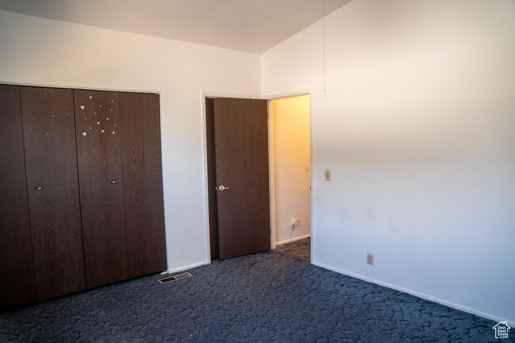 Unfurnished bedroom featuring dark colored carpet, a closet, and baseboards