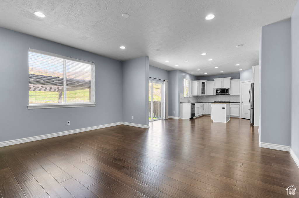 Unfurnished living room with baseboards, recessed lighting, a textured ceiling, dark wood-style flooring, and a sink
