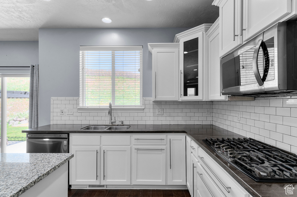 Kitchen featuring stainless steel appliances, a sink, white cabinets, glass insert cabinets, and dark stone counters