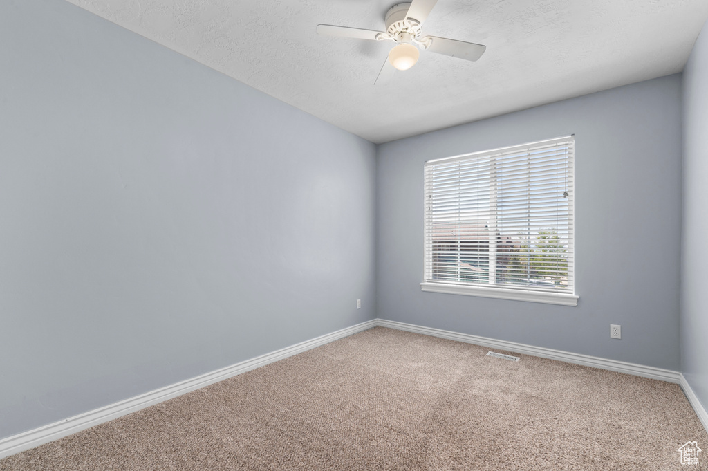 Carpeted spare room featuring baseboards, a ceiling fan, and a textured ceiling