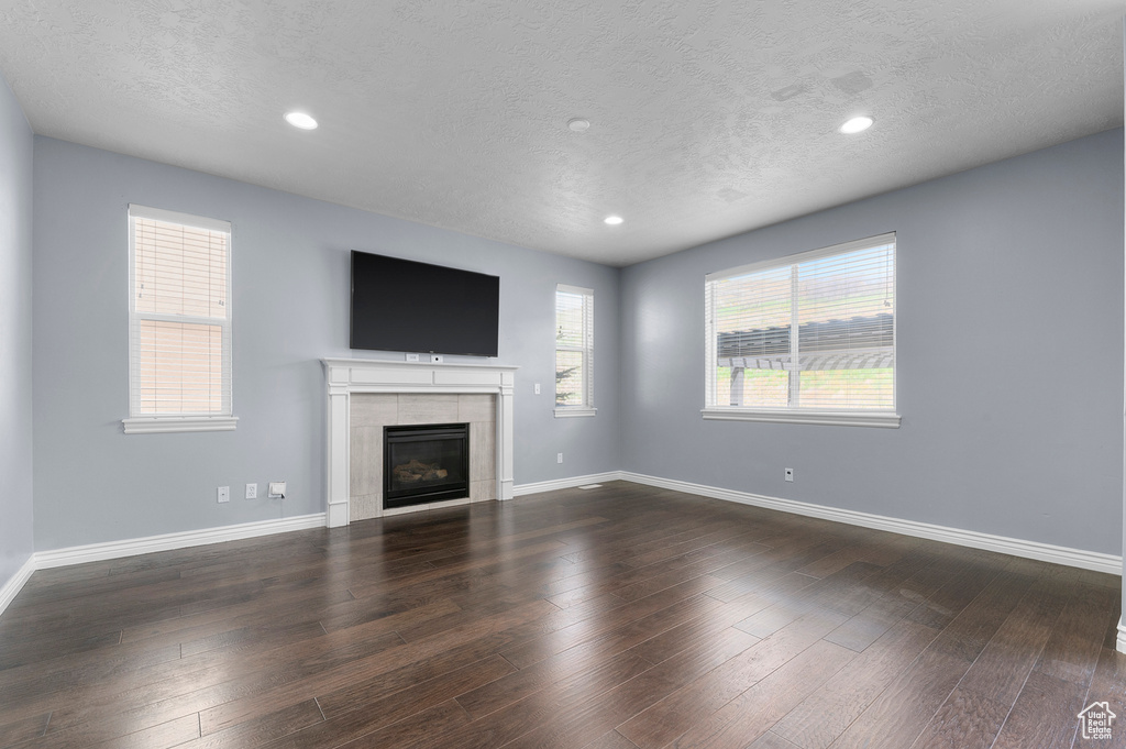 Unfurnished living room with a textured ceiling, a tiled fireplace, baseboards, recessed lighting, and dark wood-type flooring
