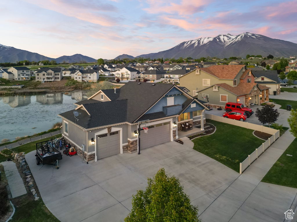 View of front of house featuring a residential view, a garage, stone siding, a water and mountain view, and driveway