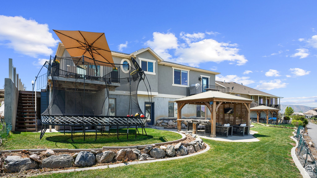 Rear view of house with a gazebo, a patio, a lawn, stucco siding, and stairs