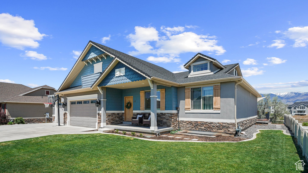 Craftsman house featuring covered porch, driveway, a mountain view, stone siding, and a garage