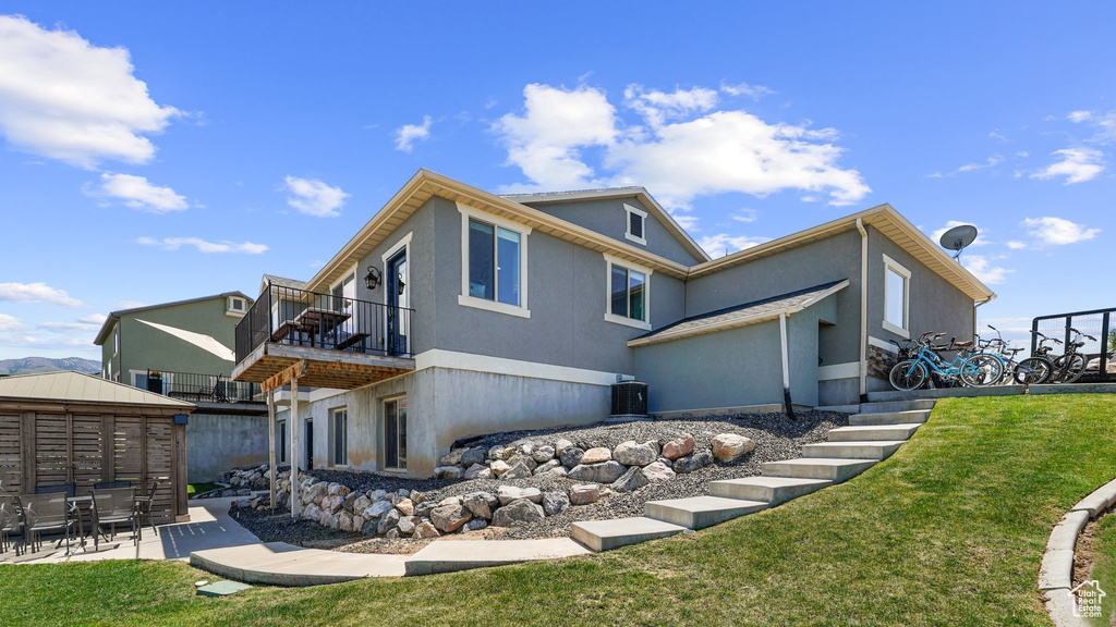 Rear view of house with a lawn, stucco siding, a patio, and a balcony