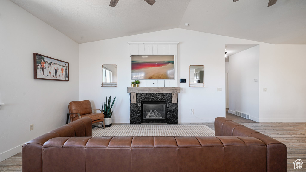 Living room featuring a ceiling fan, vaulted ceiling, wood finished floors, baseboards, and a fireplace