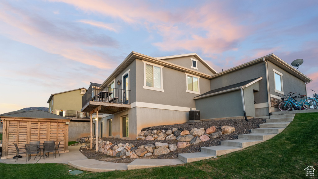 Back of property featuring stucco siding, a patio area, a lawn, a balcony, and an outdoor structure