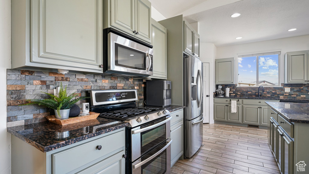 Kitchen with appliances with stainless steel finishes, gray cabinets, decorative backsplash, dark stone countertops, and recessed lighting