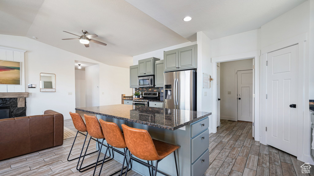 Kitchen with appliances with stainless steel finishes, light wood finished floors, ceiling fan, a kitchen bar, and vaulted ceiling