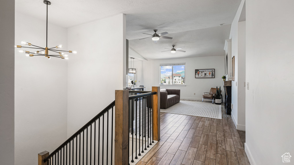 Hallway with an upstairs landing, dark wood finished floors, baseboards, a chandelier, and vaulted ceiling