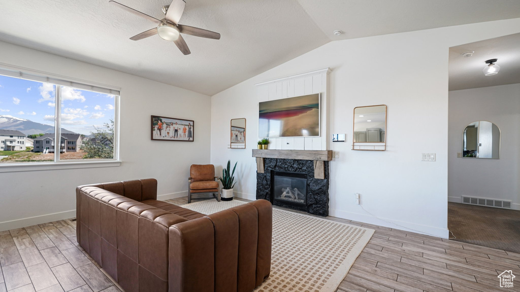 Living room featuring a ceiling fan, light wood-style flooring, lofted ceiling, a fireplace, and baseboards