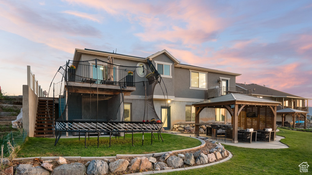Back of house at dusk with a gazebo, a yard, stucco siding, stairway, and a patio area