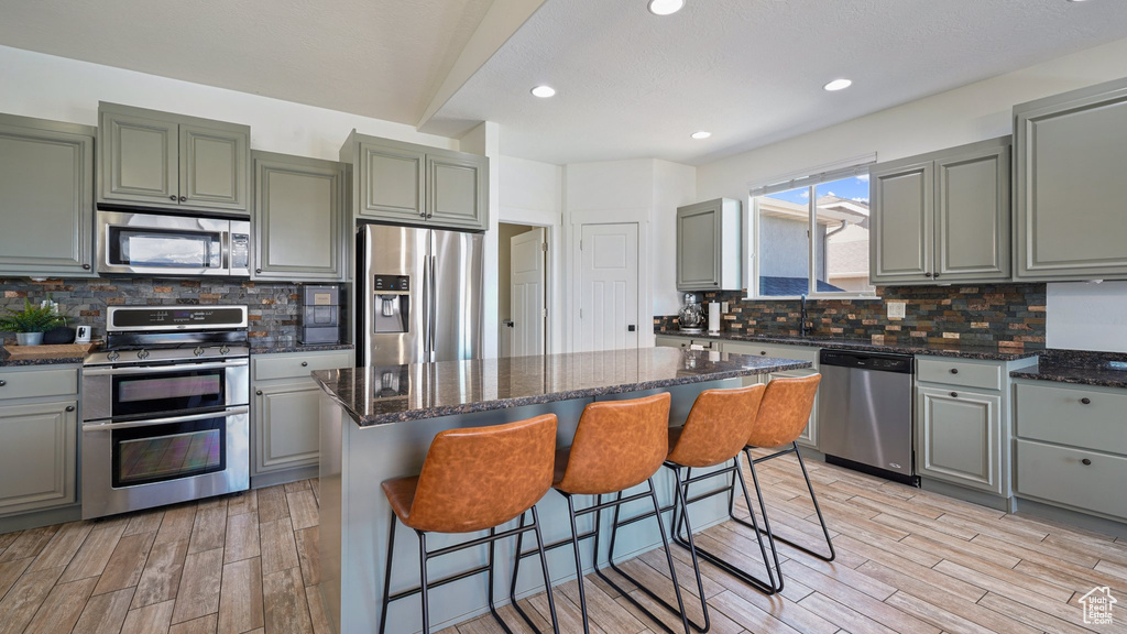 Kitchen with stainless steel appliances, light wood-type flooring, gray cabinetry, tasteful backsplash, and recessed lighting