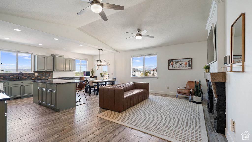 Living area featuring a ceiling fan, wood finished floors, lofted ceiling, baseboards, and a fireplace