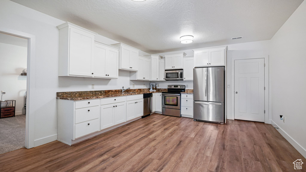 Kitchen featuring stainless steel appliances, white cabinetry, baseboards, wood finished floors, and dark stone counters