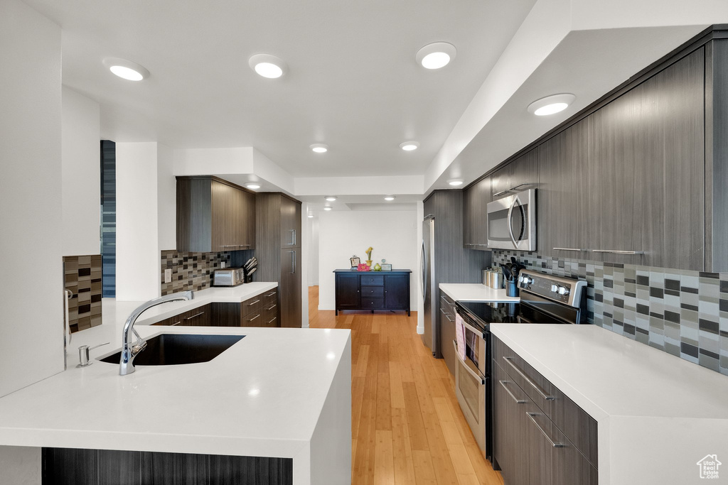 Kitchen with stainless steel appliances, a sink, tasteful backsplash, light countertops, and recessed lighting