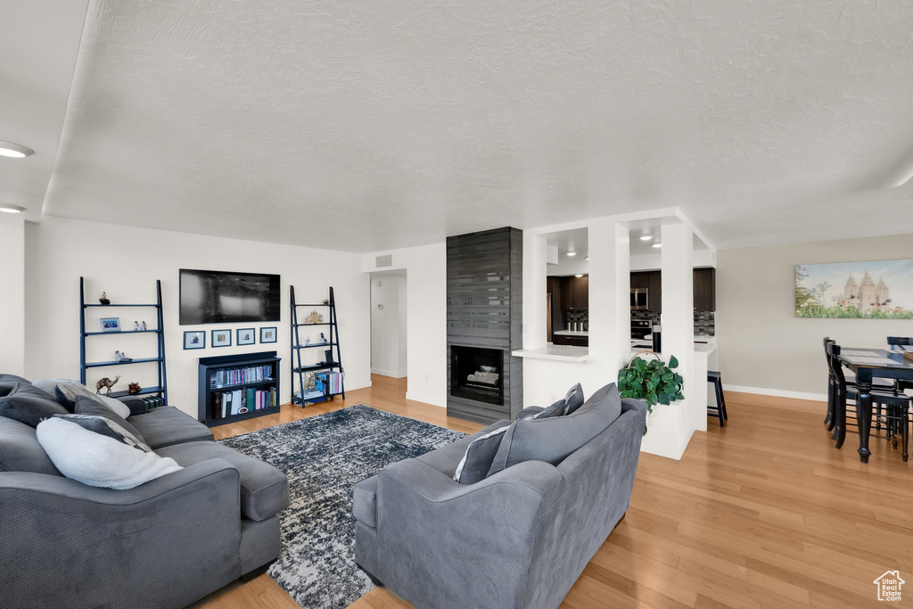 Living area with a fireplace, baseboards, light wood finished floors, and a textured ceiling