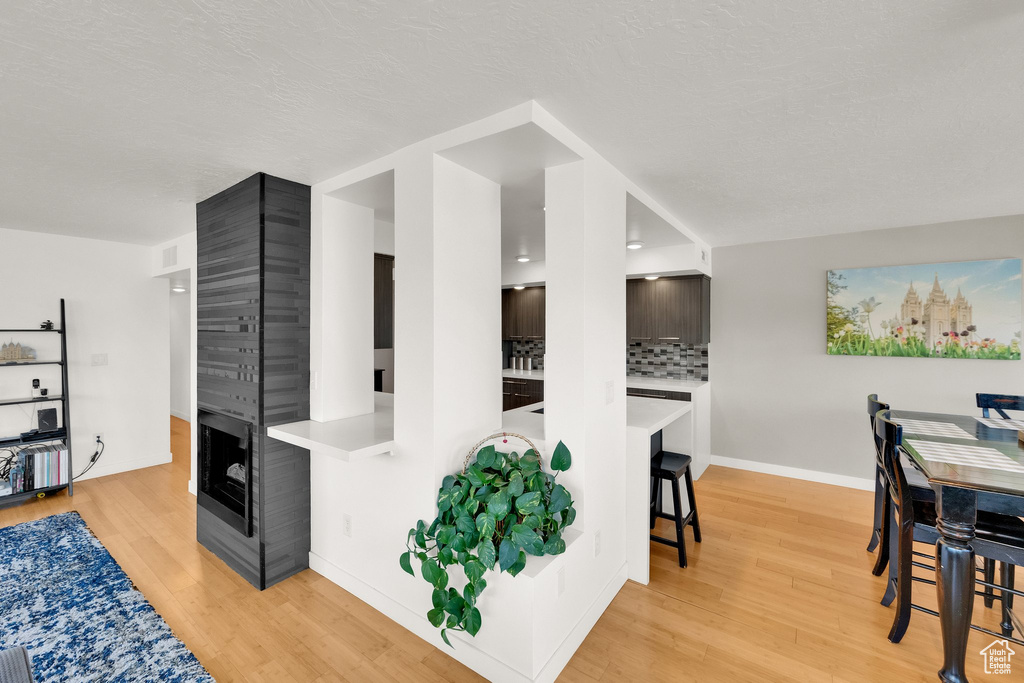 Kitchen with light countertops, light wood-type flooring, backsplash, a multi sided fireplace, and baseboards