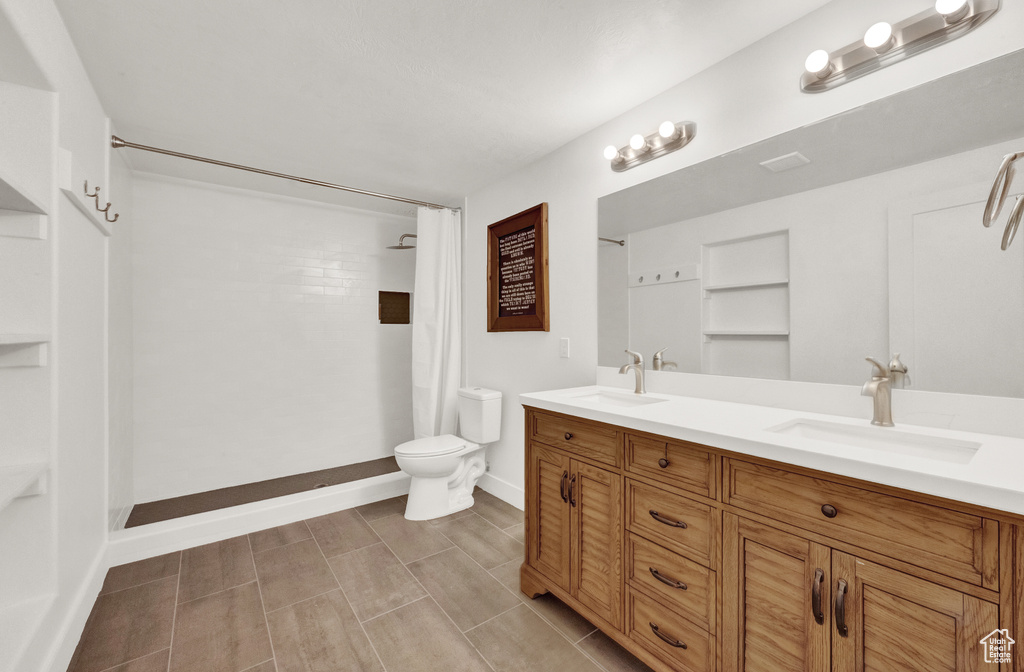 Bathroom featuring toilet, double vanity, baseboards, and a shower with shower curtain