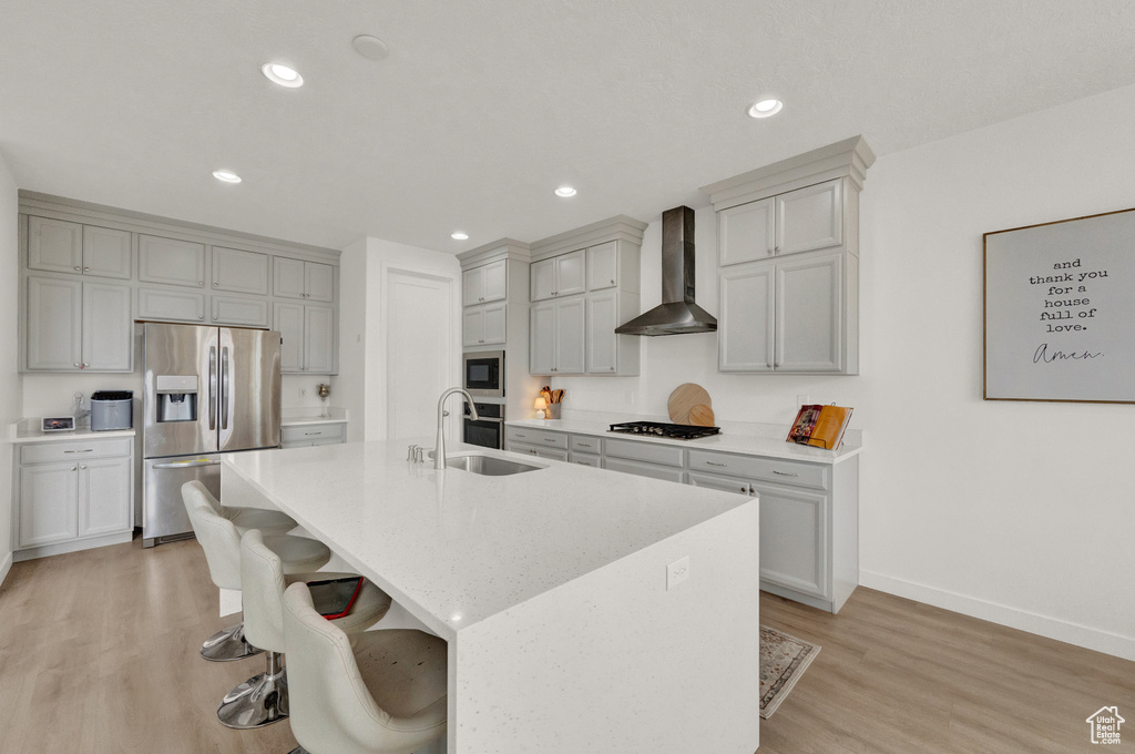 Kitchen with appliances with stainless steel finishes, wall chimney exhaust hood, light wood-style flooring, a kitchen breakfast bar, and recessed lighting