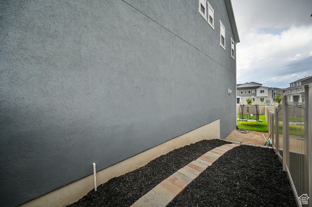 View of side of home featuring a trampoline, stucco siding, a residential view, and fence