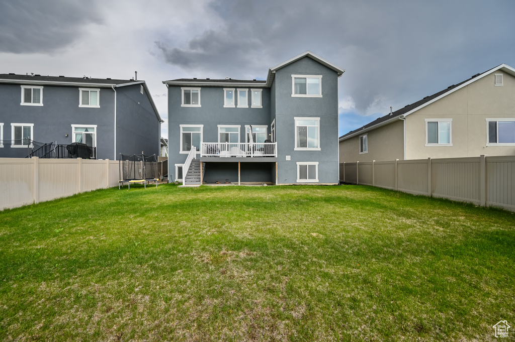 Rear view of property featuring a trampoline, a deck, stairway, and stucco siding