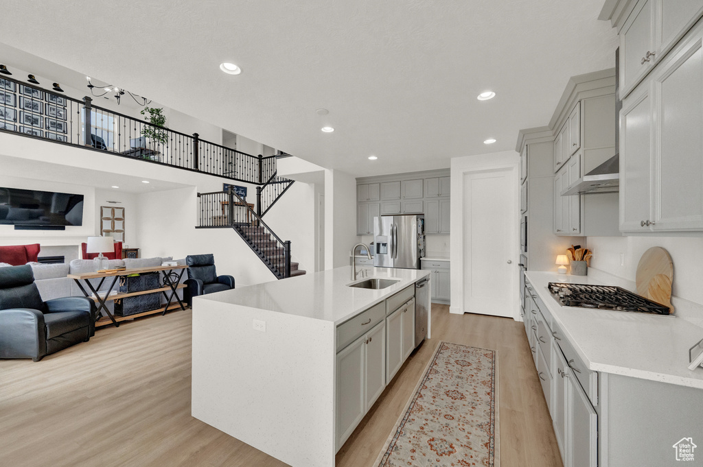 Kitchen with stainless steel appliances, a sink, open floor plan, gray cabinets, and light wood-style flooring
