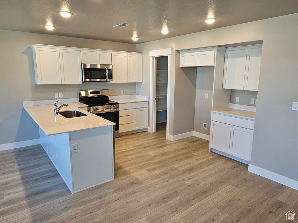 Kitchen featuring appliances with stainless steel finishes, a sink, baseboards, a peninsula, and white cabinetry