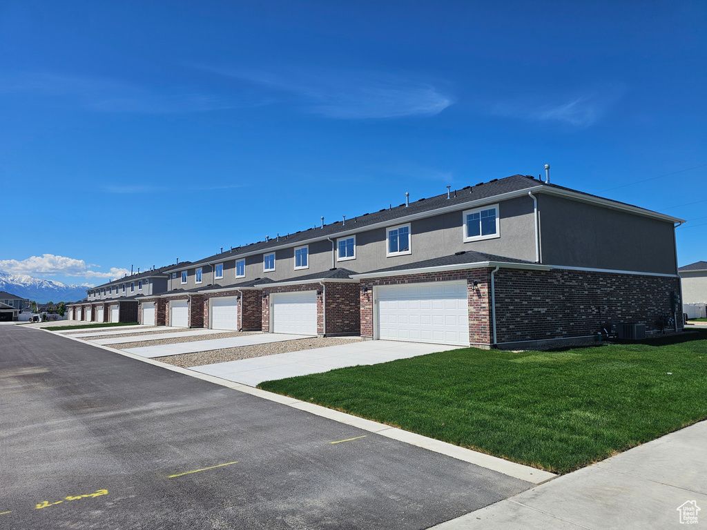Townhome / multi-family property with stucco siding, a front yard, central AC unit, brick siding, and a garage