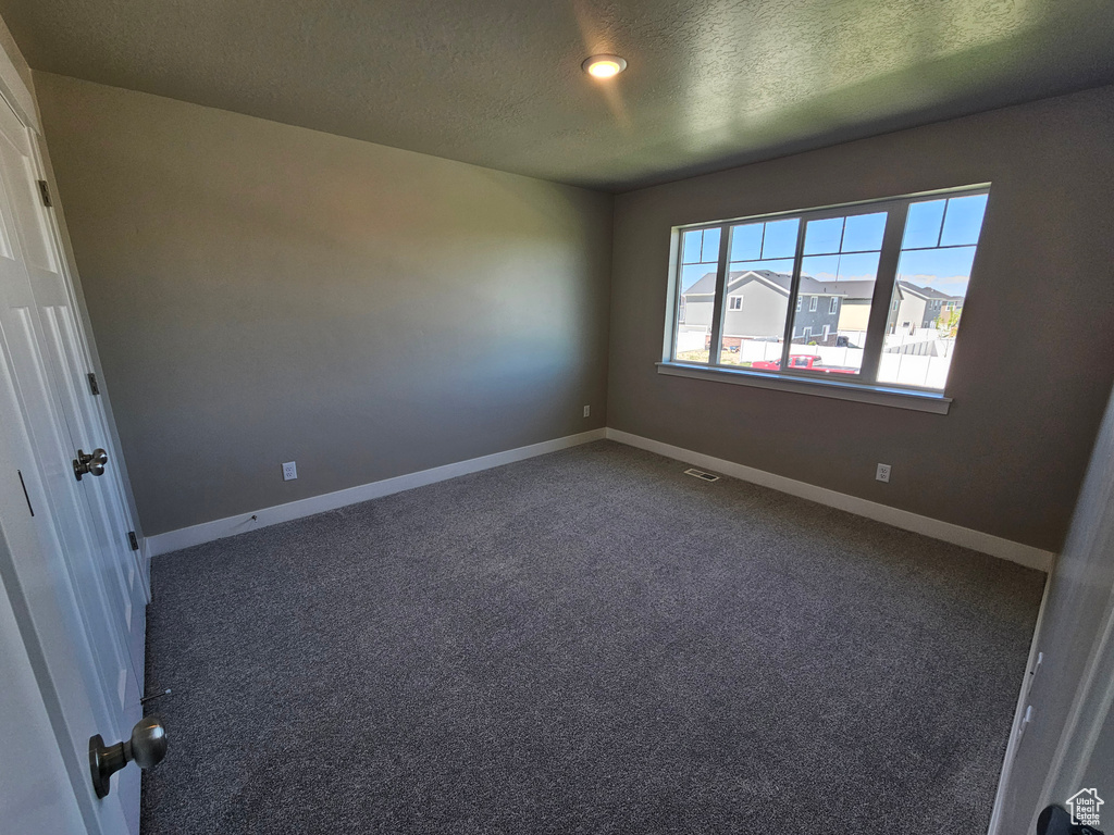 Empty room with a textured ceiling, carpet flooring, and baseboards