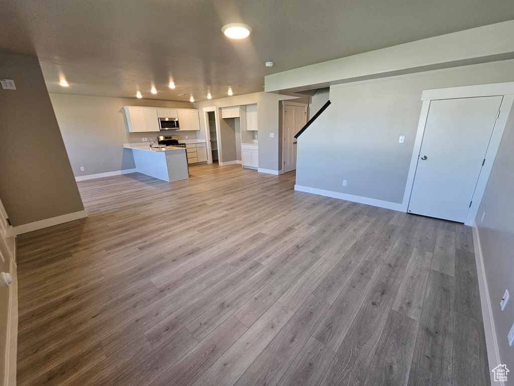Unfurnished living room featuring light wood-type flooring and baseboards