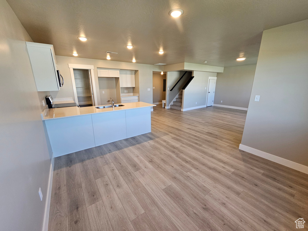 Kitchen with white cabinetry, a peninsula, baseboards, a sink, and light countertops