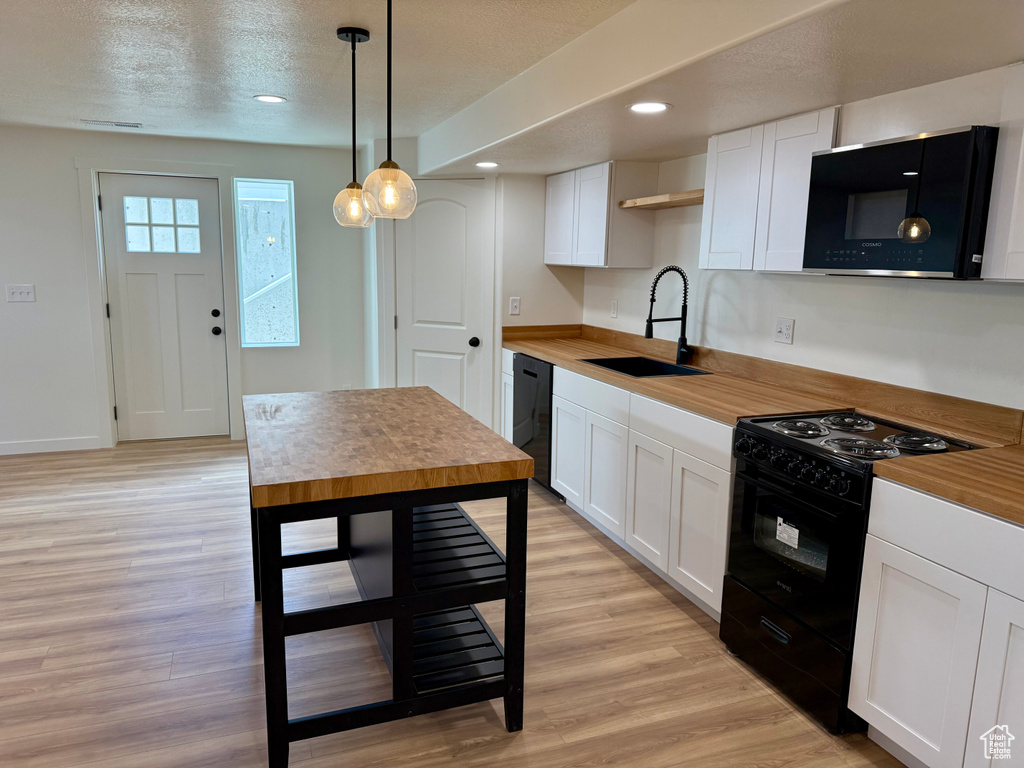 Kitchen with black appliances, white cabinets, light wood-style floors, decorative light fixtures, and recessed lighting