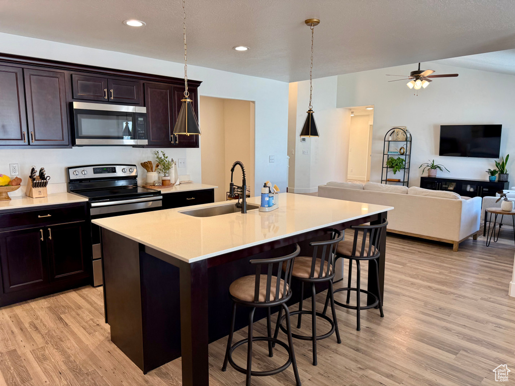 Kitchen featuring appliances with stainless steel finishes, a sink, a kitchen breakfast bar, light wood finished floors, and recessed lighting