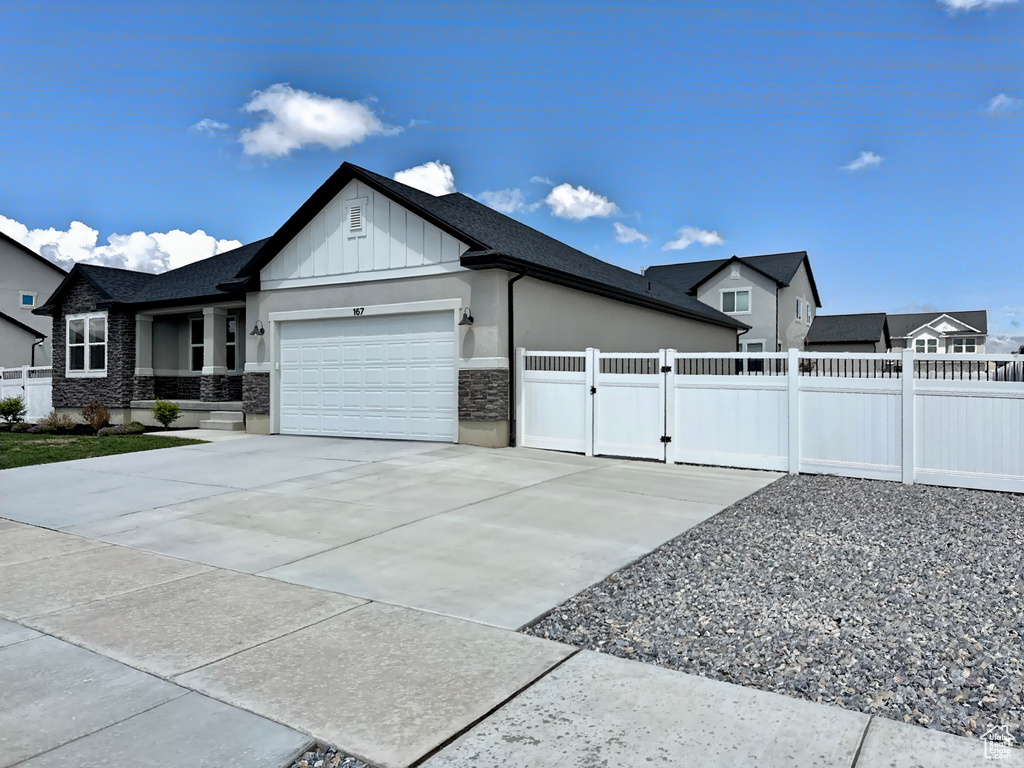 View of side of home featuring an attached garage, fence, board and batten siding, a gate, and concrete driveway