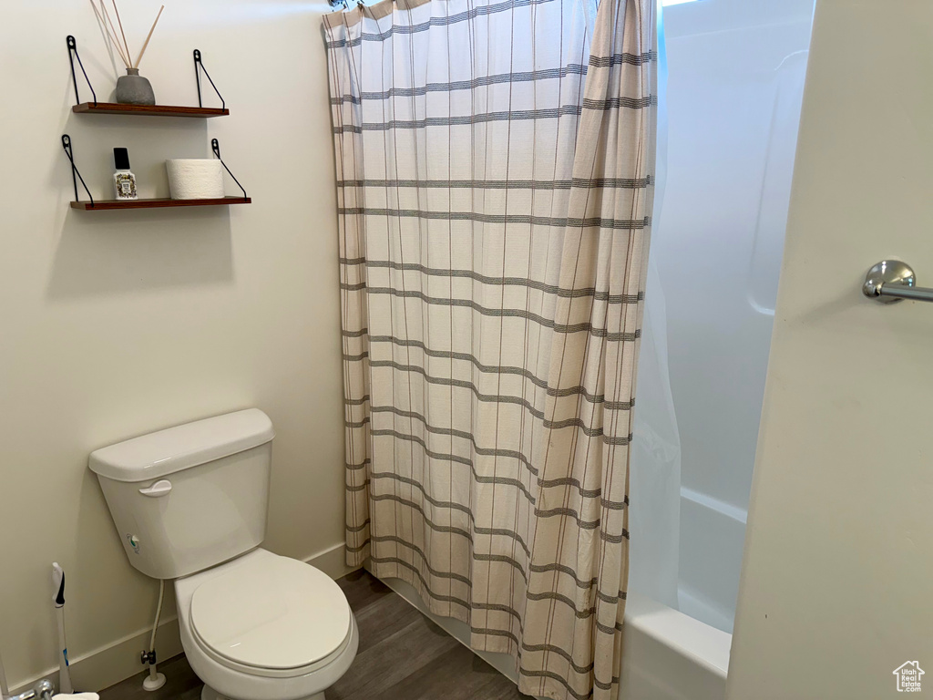 Full bathroom featuring toilet, wood finished floors, and shower / bath combination with curtain