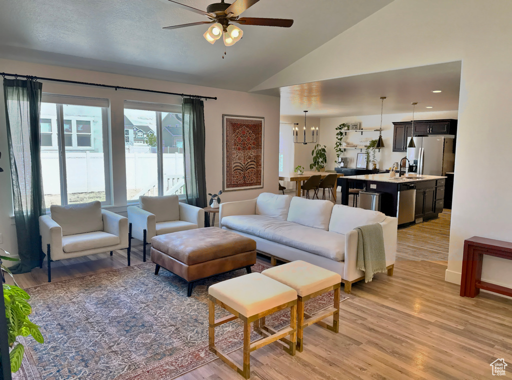 Living room featuring a ceiling fan, light wood-style flooring, lofted ceiling, and a chandelier