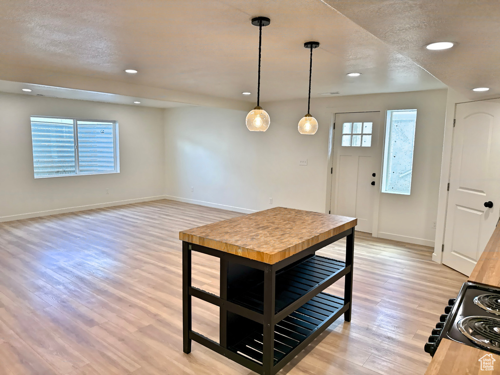 Kitchen with baseboards, black range with electric cooktop, light wood-type flooring, recessed lighting, and hanging light fixtures